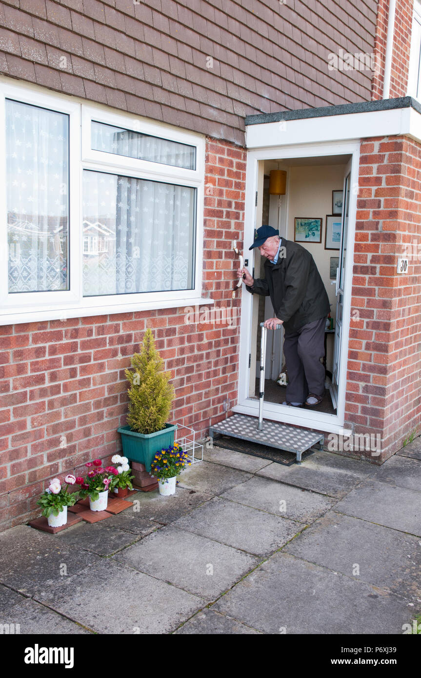 Uomo anziano di uscire dalla sua casa su un anti-slittamento metà esterna-fase, utilizzando un bastone e maniglia di sostegno Foto Stock