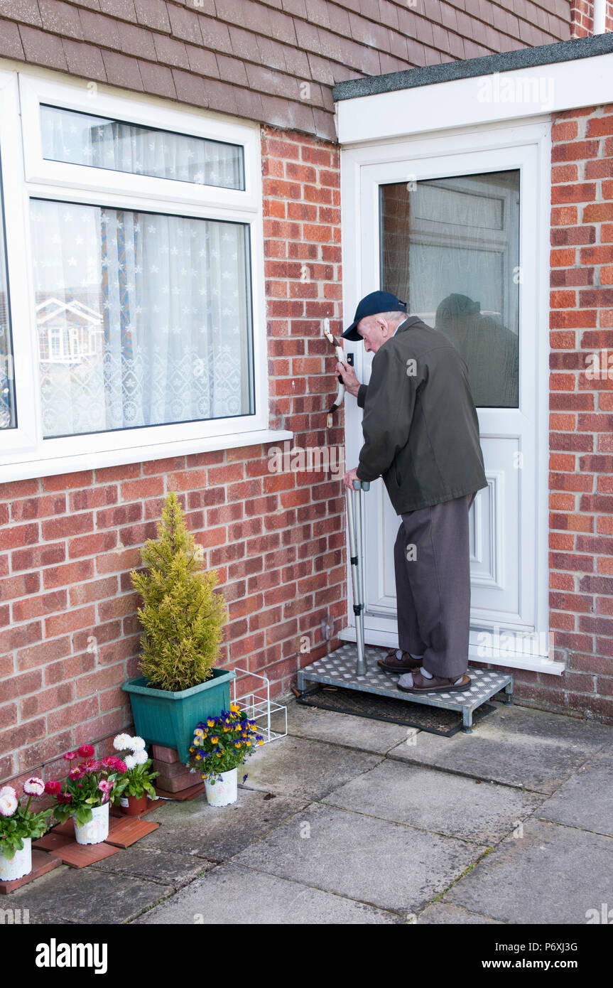 Uomo anziano di uscire dalla sua casa su un anti-slittamento metà esterna-fase, utilizzando un bastone e maniglia di sostegno Foto Stock