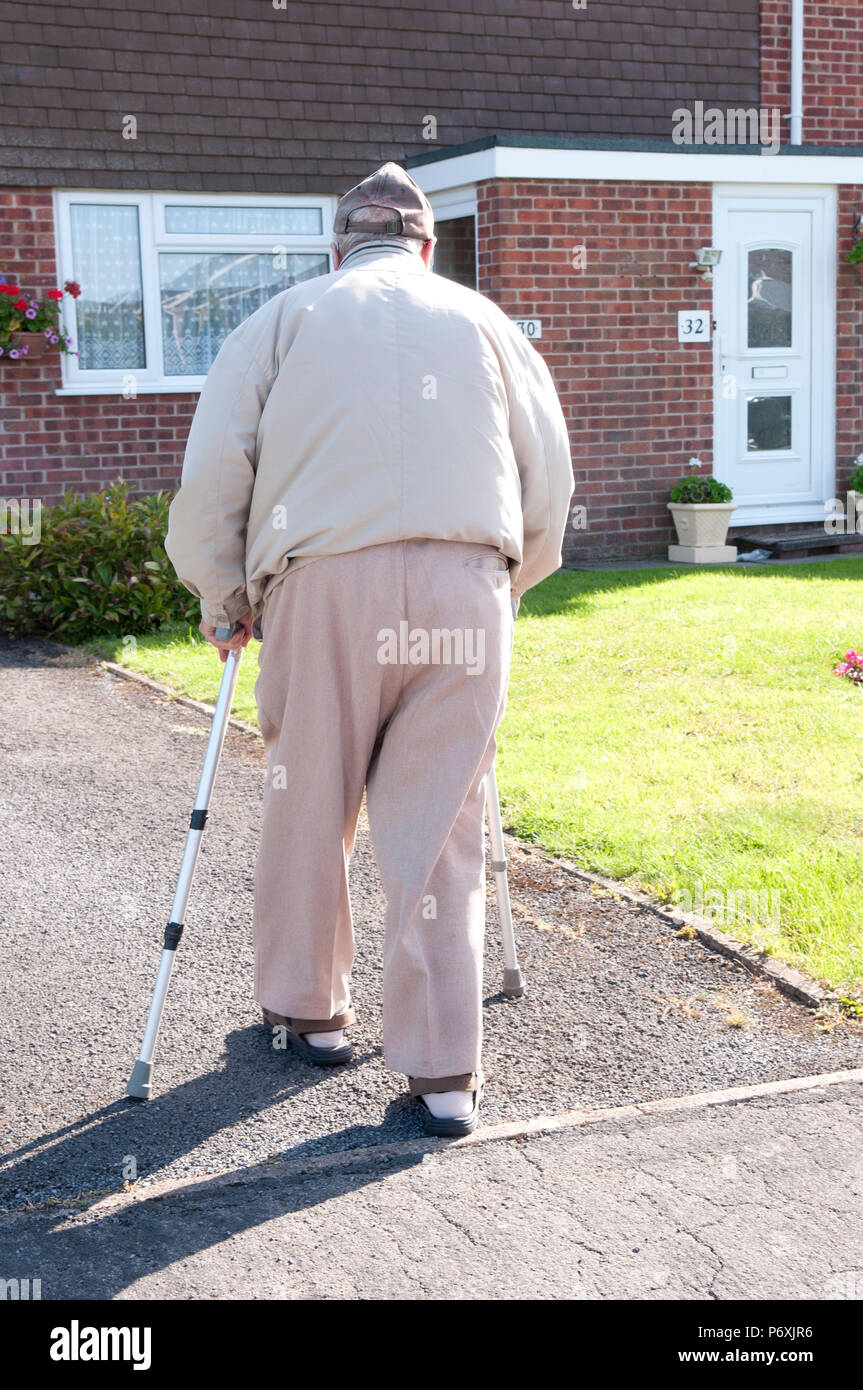 Vista posteriore di uomo anziano con bastoni da passeggio in cammino verso la sua casa Foto Stock
