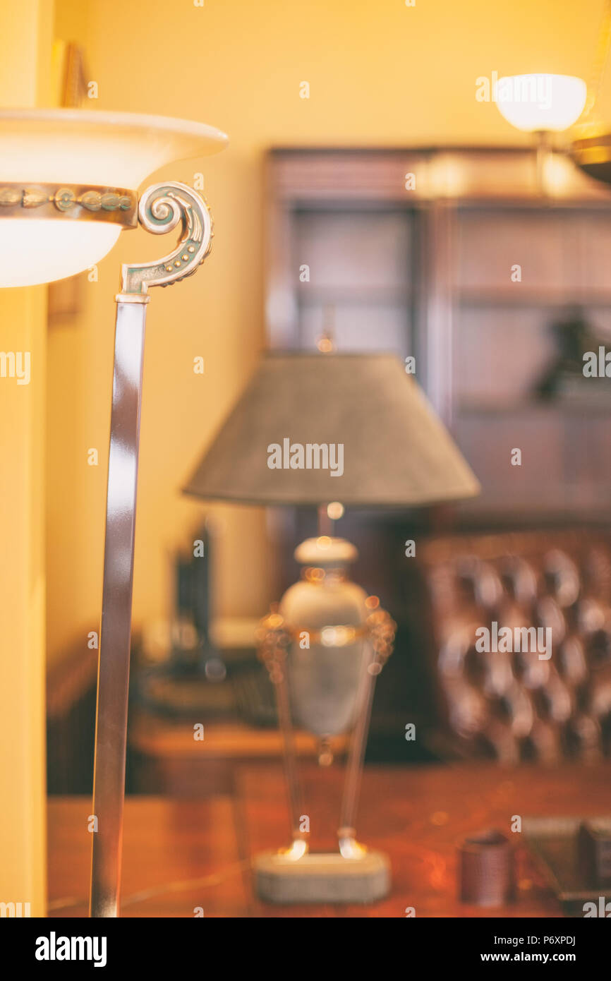 Una lampada con una sfumatura sorge su una tabella sullo sfondo di una sedia in pelle in un ambiente ricco di atmosfera Foto Stock
