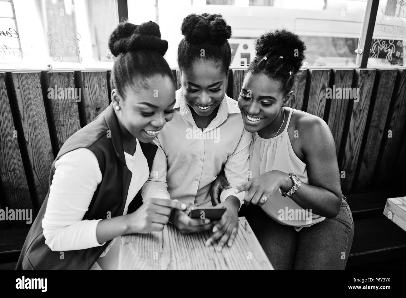 Tre African American ragazze seduta sul tavolo del caffe e guardando sul telefono cellulare. Foto Stock