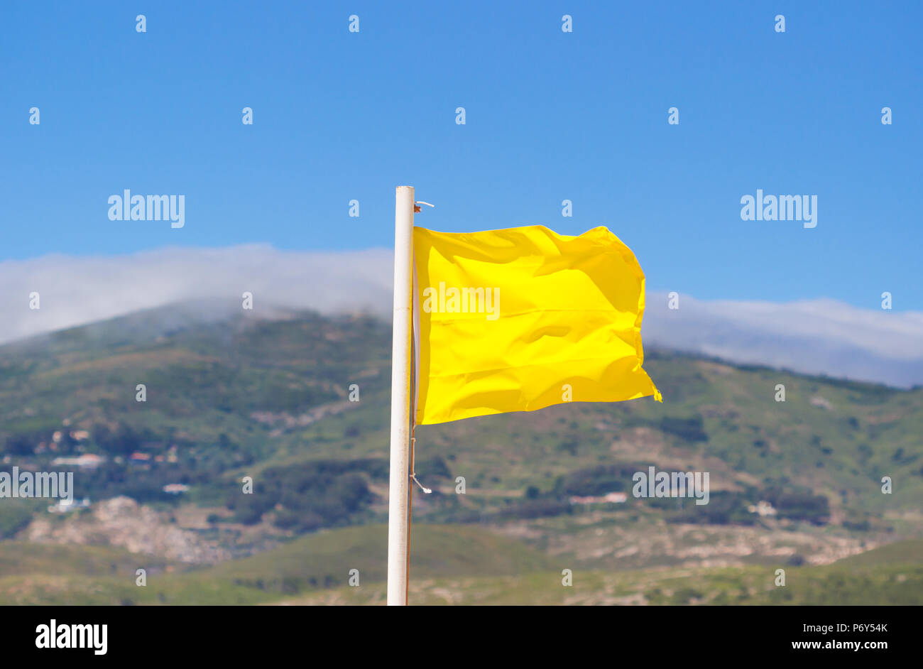 Bandiera gialla sventola sulla spiaggia di La brezza contro una offuscata blue sky. Foto Stock