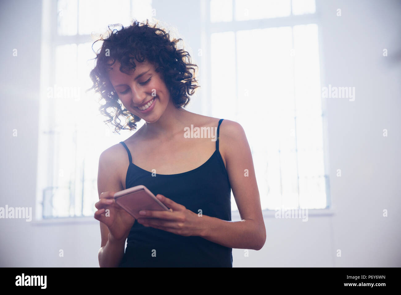 Sorridente giovane ballerino femmina texting con smart phone in studio di danza Foto Stock