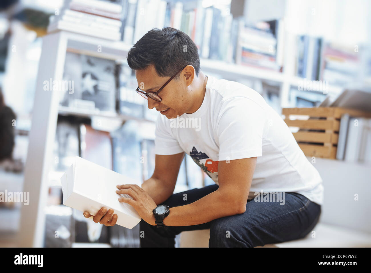 Giovani spectacled brunette uomo seduto e la lettura del libro bianco con coperchio. Foto Stock