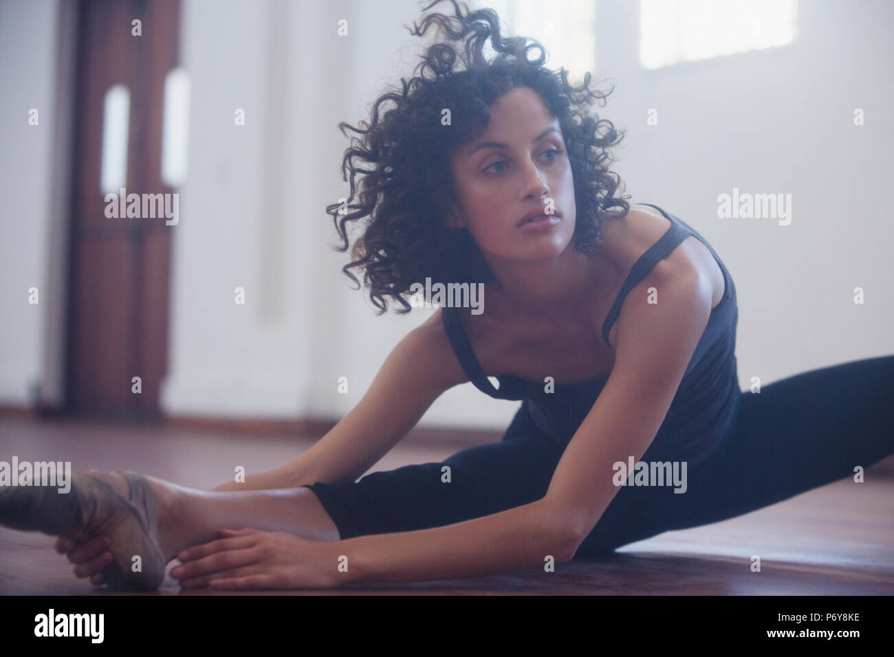 Focalizzato giovane ballerino femmina allungamento della gamba in studio di danza Foto Stock