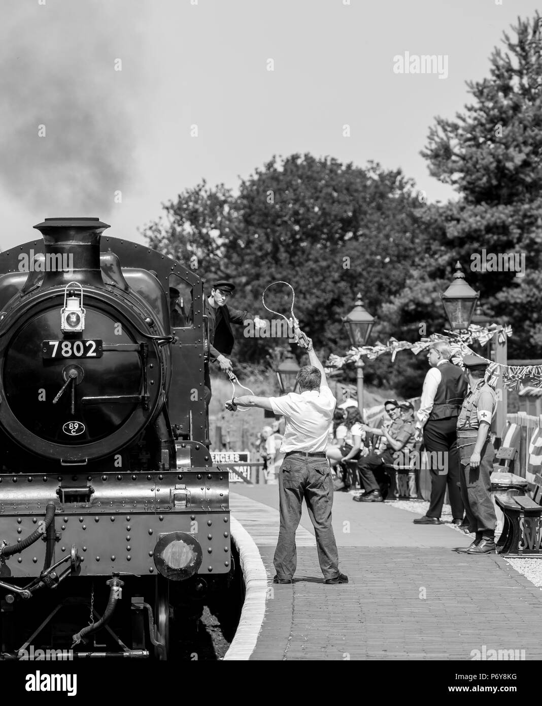 Un passo indietro a 1940s weekend: vintage locomotore cuoce a vapore nella stazione di Arley come segnalatore attende sulla piattaforma pronta per lo scambio token con equipaggio di cabina. Foto Stock