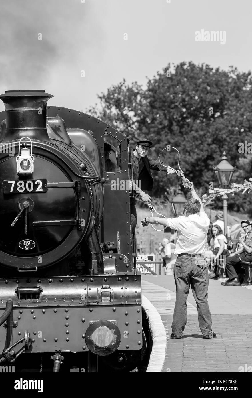 Un passo indietro a 1940s weekend: vintage locomotore cuoce a vapore nella stazione di Arley come segnalatore attende sulla piattaforma pronta per lo scambio token con vigile del fuoco. Foto Stock