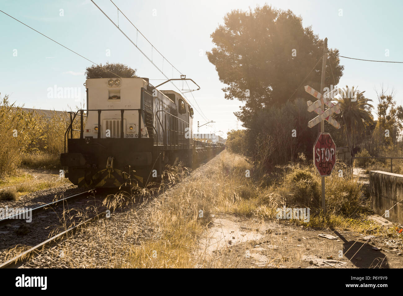 Passaggio a livello senza barriere con un simbolo di arresto, mentre il passaggio di un treno merci. Sagunto, Valencia, Spagna Foto Stock