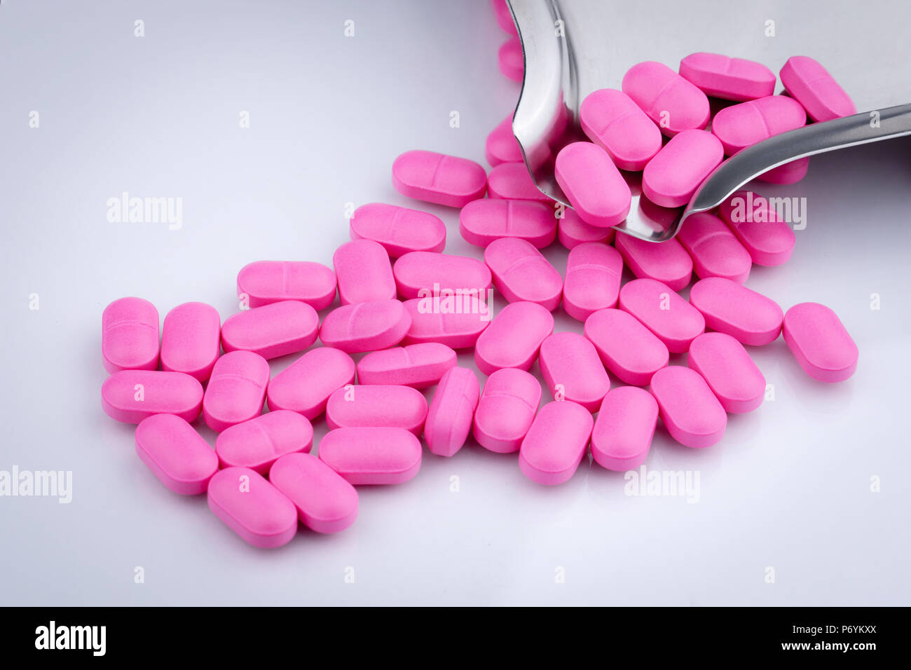 Pila di compresse di colore rosa confetto su sfondo bianco nei pressi di  acciaio inossidabile farmaco vassoio. Norfloxacin 400 mg per il trattamento  la cistite. Antibiotici la resistenza al farmaco Foto stock -