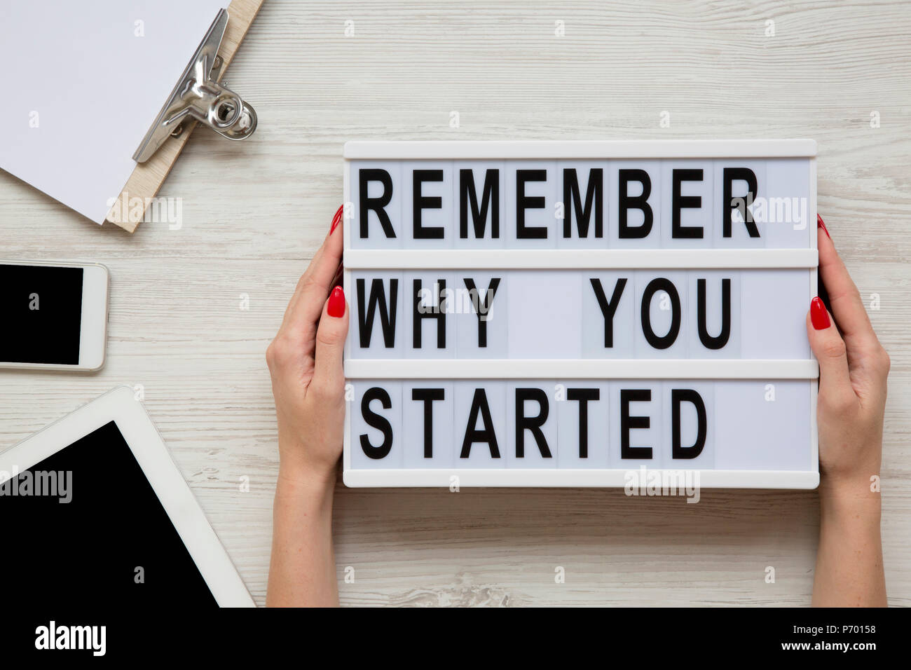 Lo spazio di lavoro con il tablet e smartphone, foglio e 'ricordate il motivo per cui si è iniziato a parole su lightbox su bianco tavolo in legno. Mani femminili tenere la scheda moderna con Foto Stock