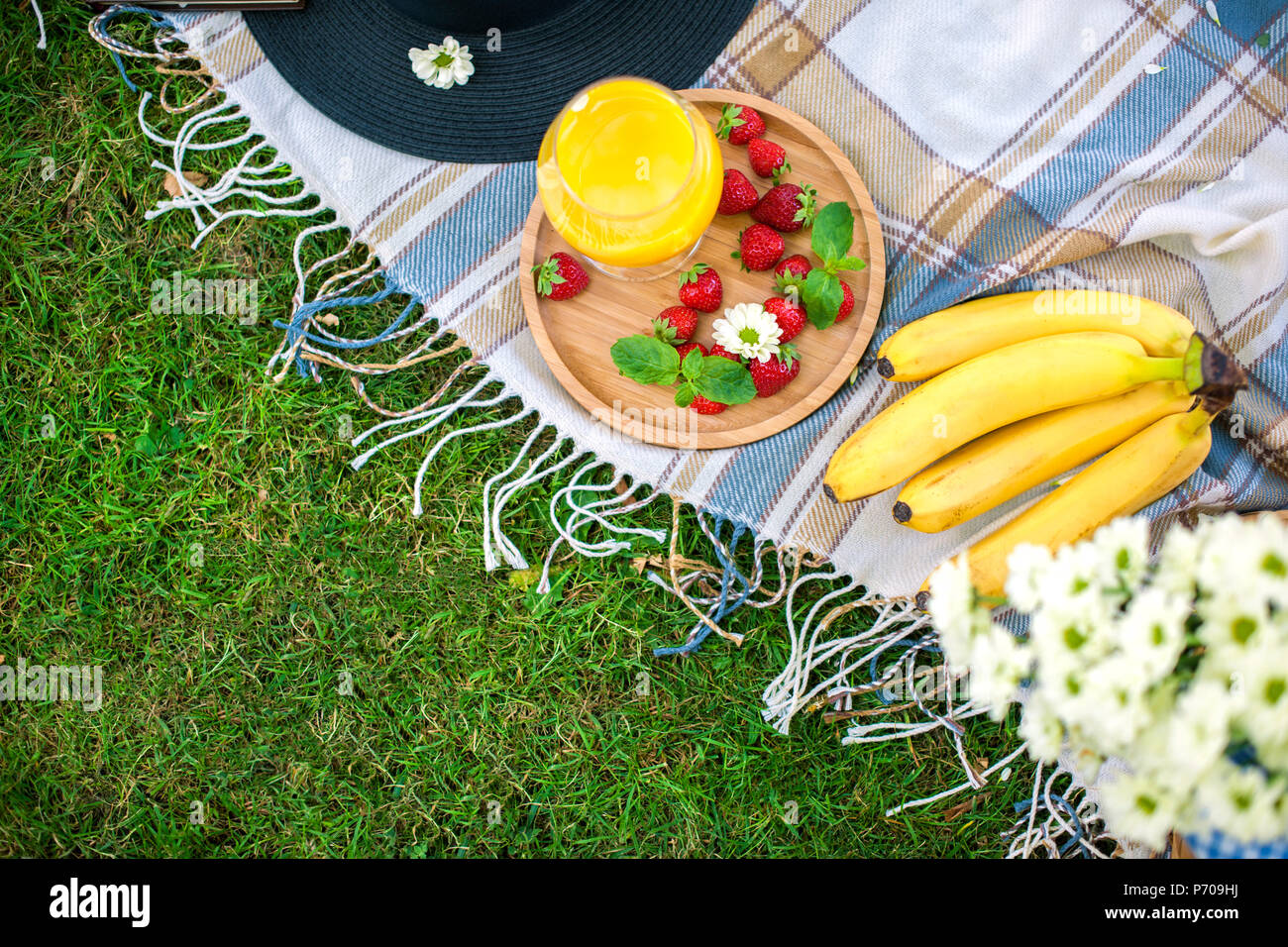 Picnic nel parco sull'erba verde, vista dall'alto. Frutti, fiori, bevande, coperta. Spazio di copia Foto Stock