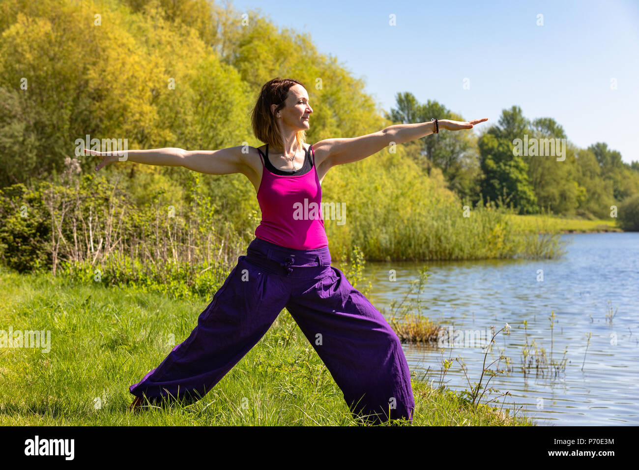 Un istruttore di yoga dimostra lo yoga pone durante un esterno di sessione di yoga in natura con il blu del cielo e colori brillanti. Foto Stock