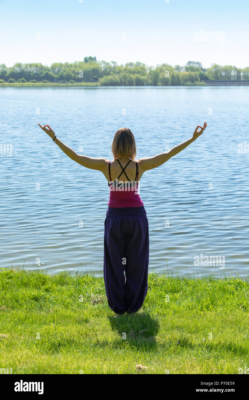 Un istruttore di yoga dimostra lo yoga pone durante un esterno di sessione di yoga in natura con il blu del cielo e colori brillanti. Foto Stock