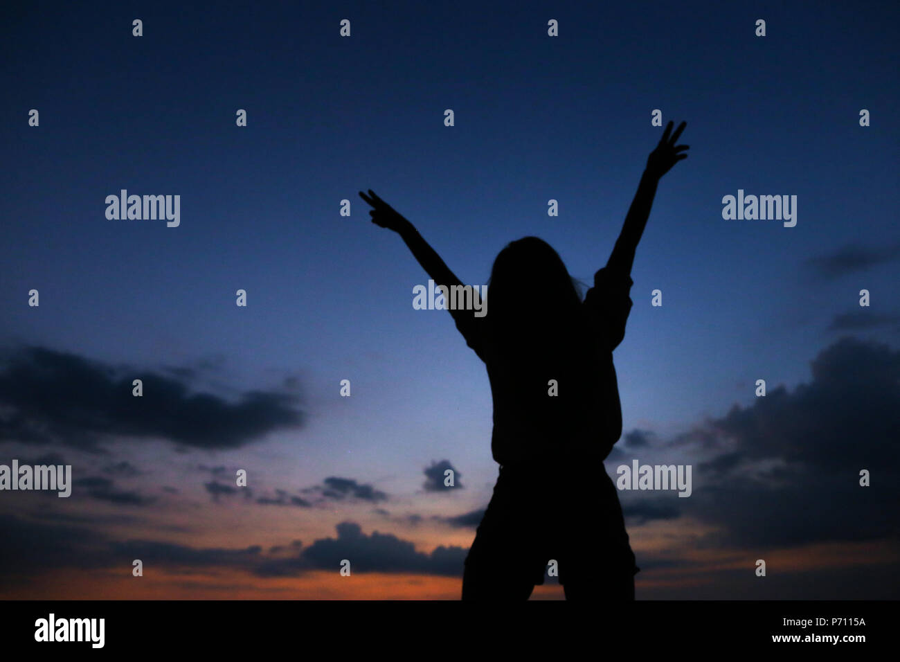 Silhouette di giovane donna nel tramonto cielo blu scuro con nuvole di sfondo. Foto Stock