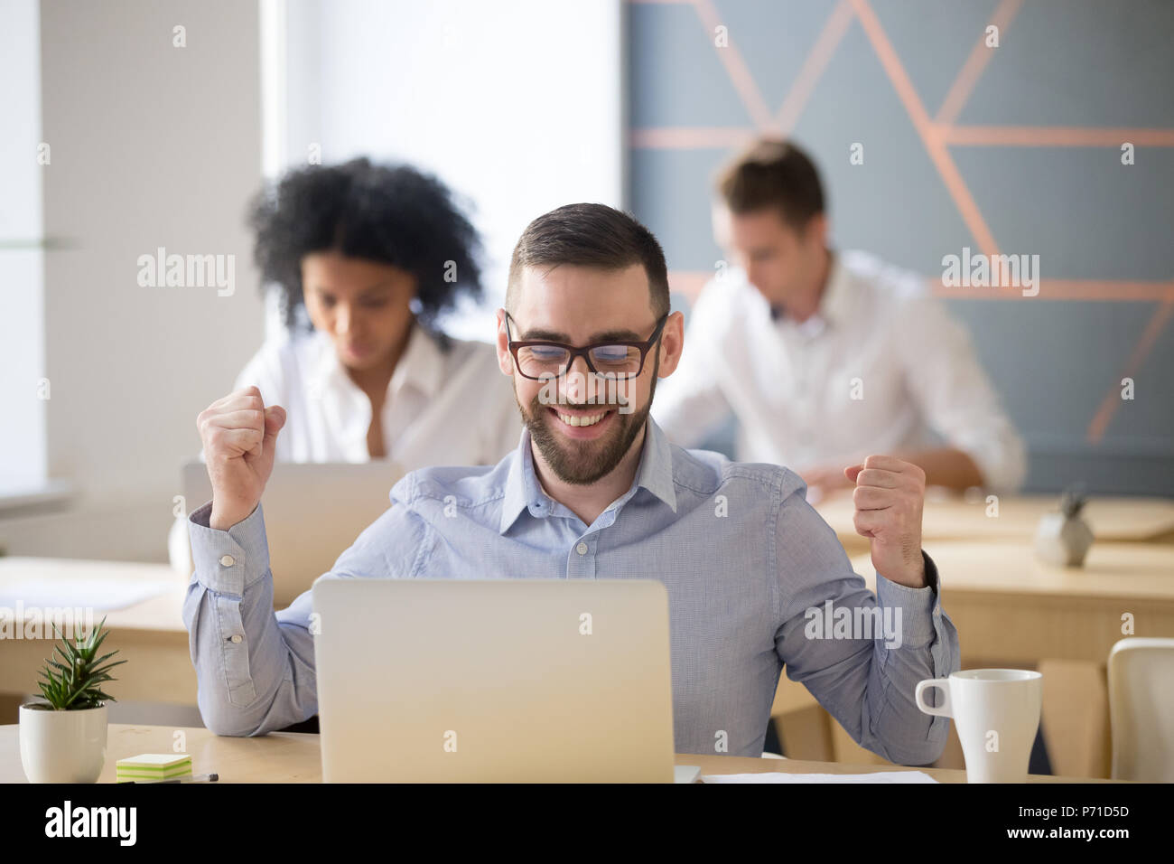 Emozionato lavoratore maschile vincente lotteria online in seduta coworking Foto Stock