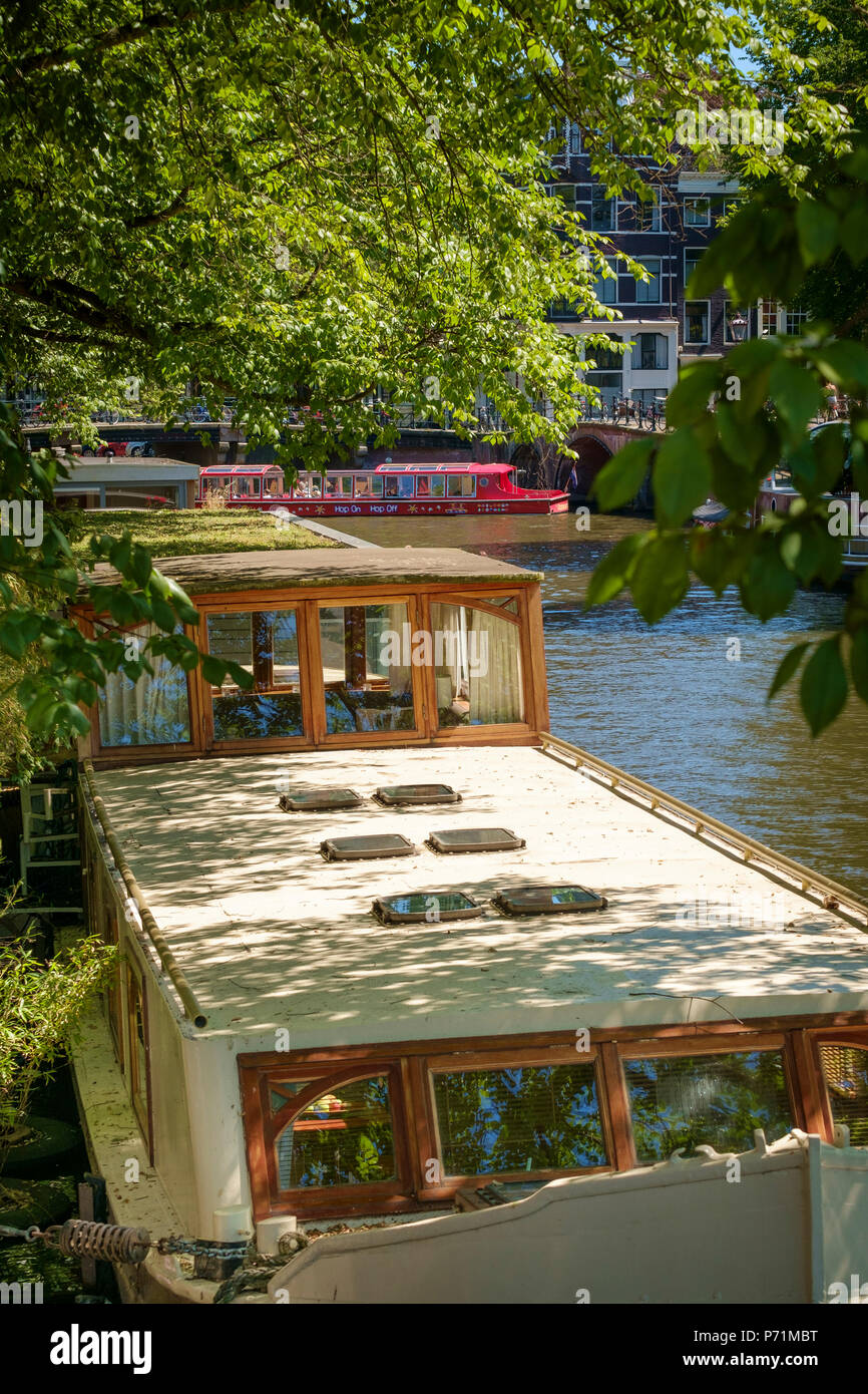 Pezzata dalla luce del sole su una Houseboat Amsterdam con una imbarcazione turistica in background. Foto Stock
