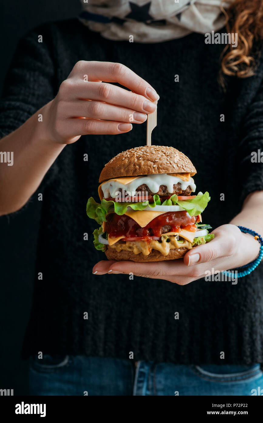 Vista ritagliata della donna grande azienda americana tradizionale cheeseburger Foto Stock