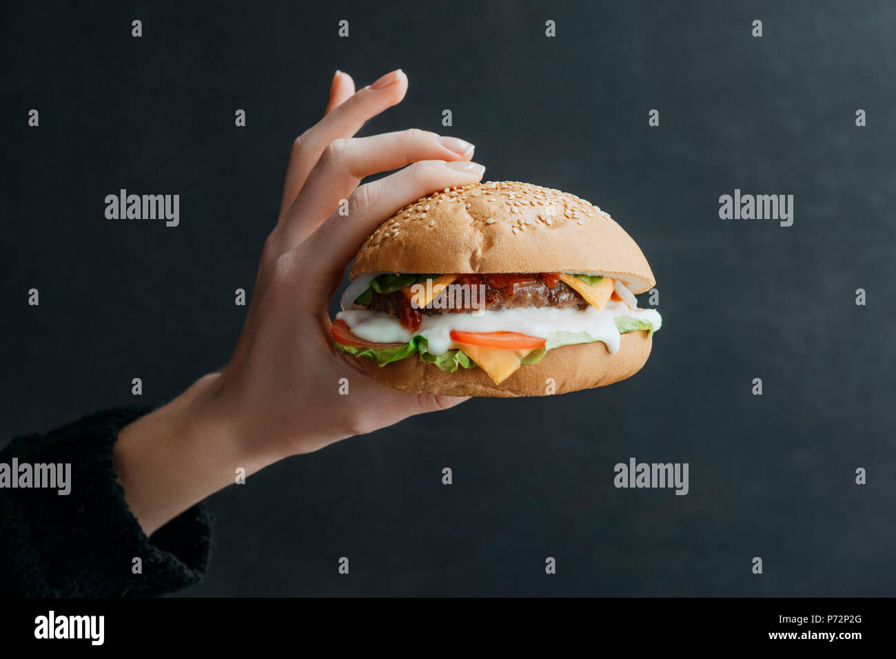 Vista ritagliata della mano con gourmet cheeseburger in casa su nero Foto Stock