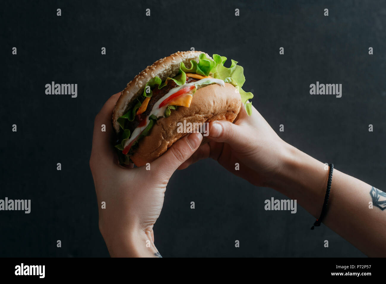Vista ritagliata della persona che mangia il gustoso cheeseburger Foto Stock