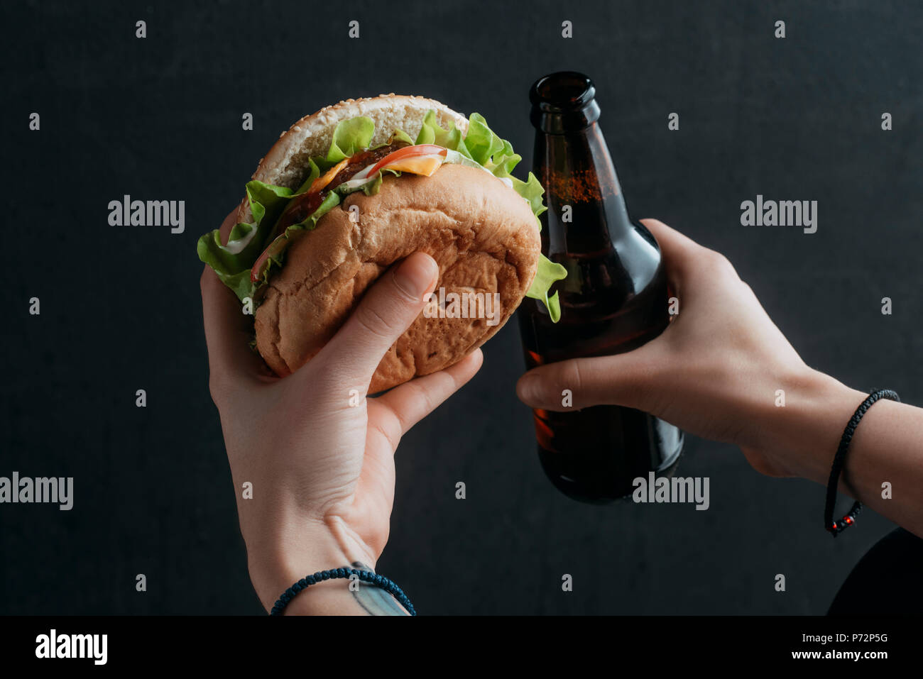 Vista ritagliata della persona in possesso di hamburger e una bottiglia di birra Foto Stock