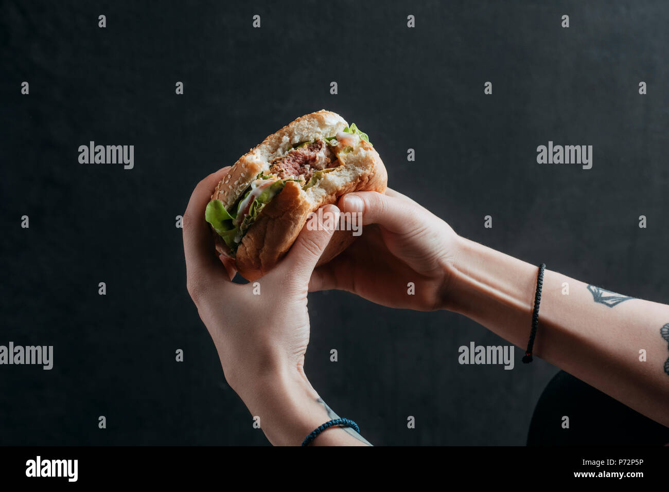 Vista ritagliata della persona che mangia hamburger gustoso Foto Stock