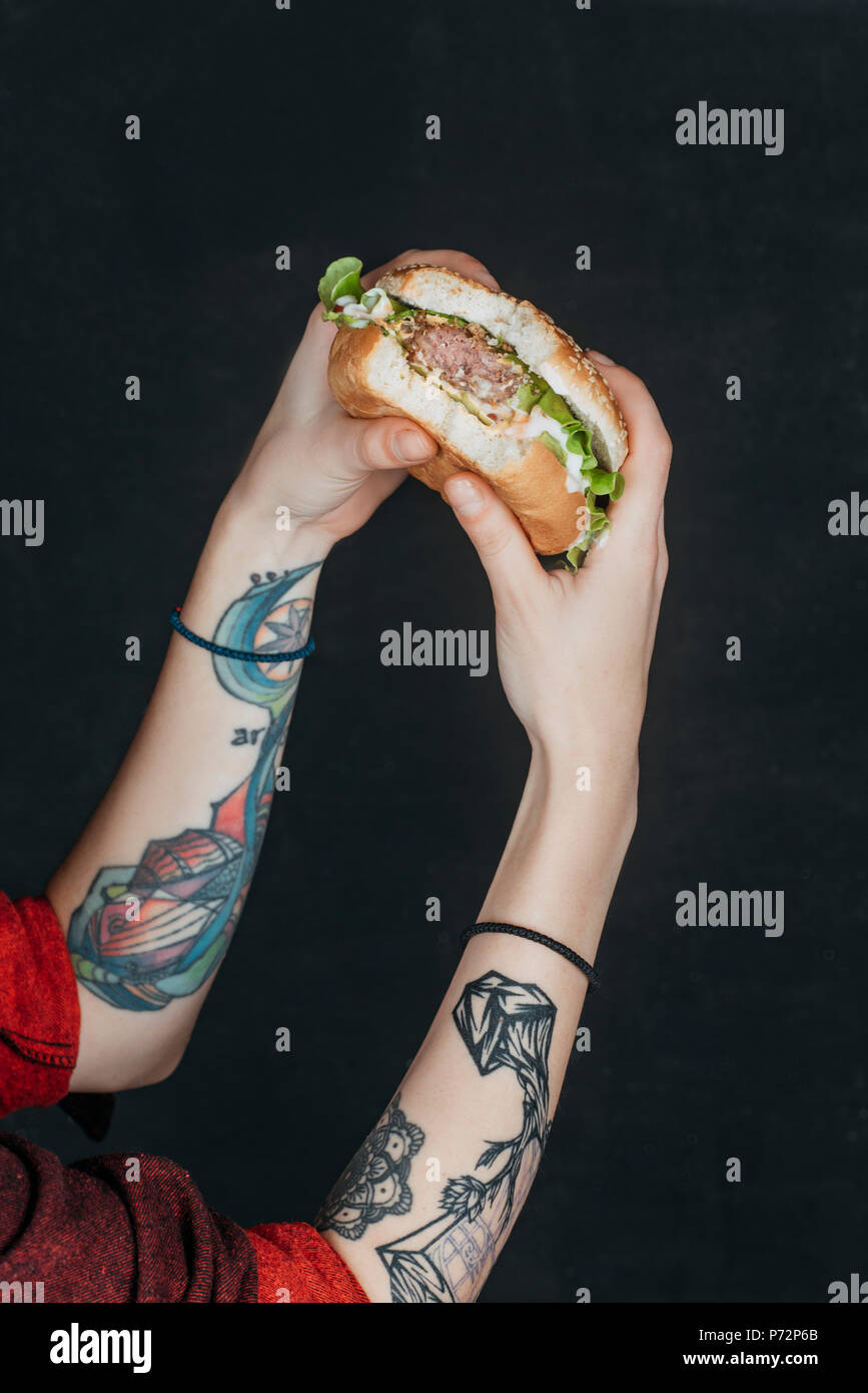 Vista ritagliata della ragazza tatuata mangiare hamburger Foto Stock