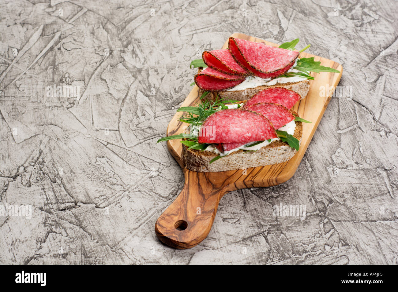 Gustosi antipasti e tagliata a fettine sottili di salame piccante su pane con formaggio ed erbe aromatiche e italiano bruschetta con erbe su un rustico sfondo di legno Foto Stock