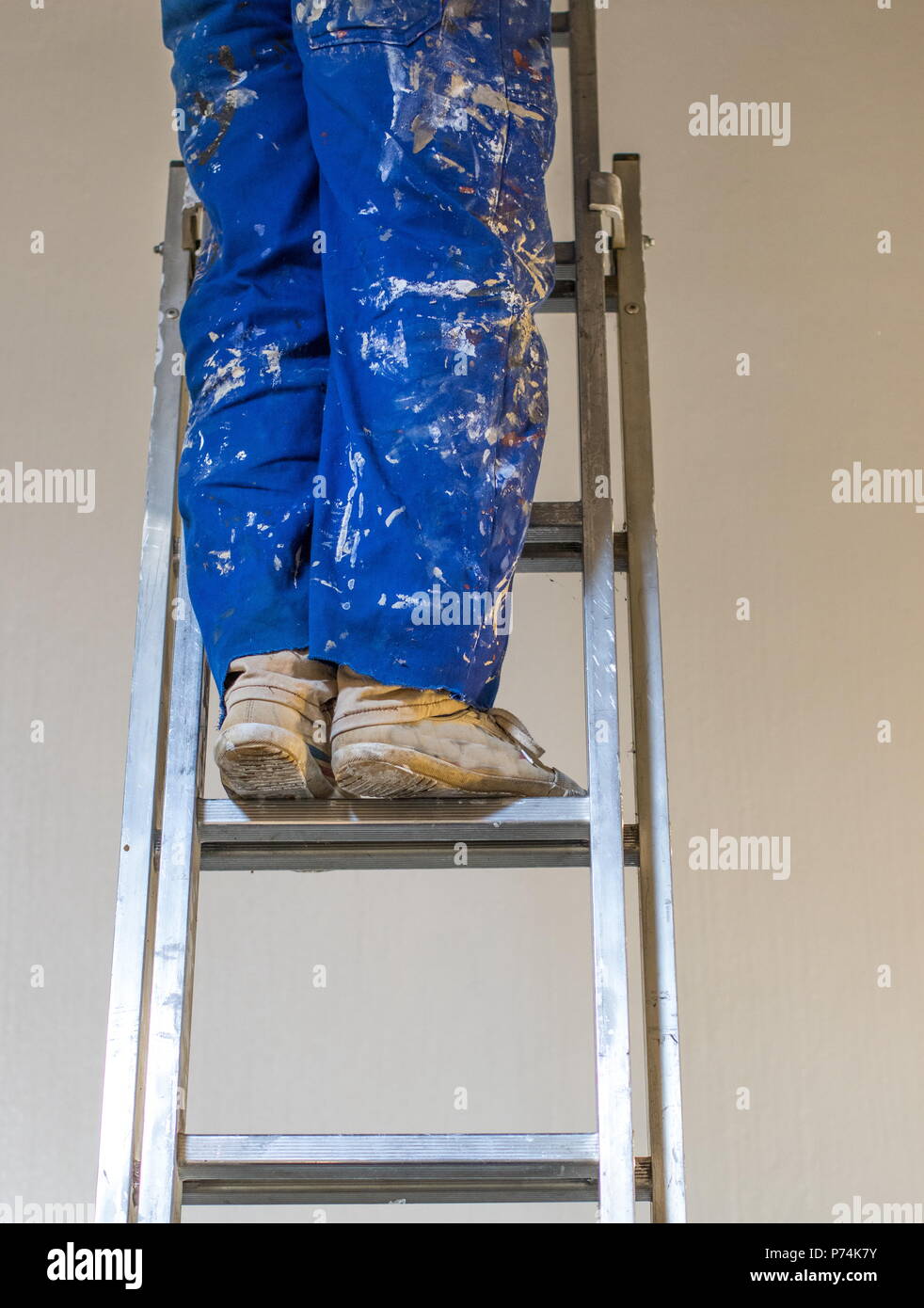 Le gambe di una persona che indossa una vernice blu-colorate nel complesso in piedi su una scala immagine con spazio copia in formato verticale Foto Stock