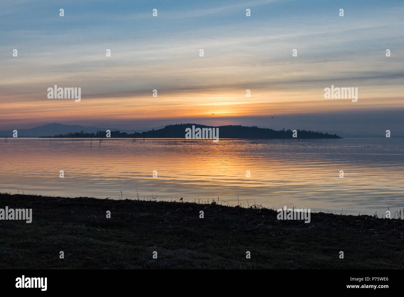 Una ripresa di un tramonto su un lago, con il sole che scende dietro un'isola Foto Stock