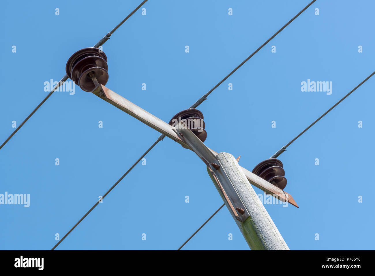 Chiusura del tettuccio di cavi di alimentazione e cavi di isolatori in cima ad un palo, contro un cielo blu Foto Stock