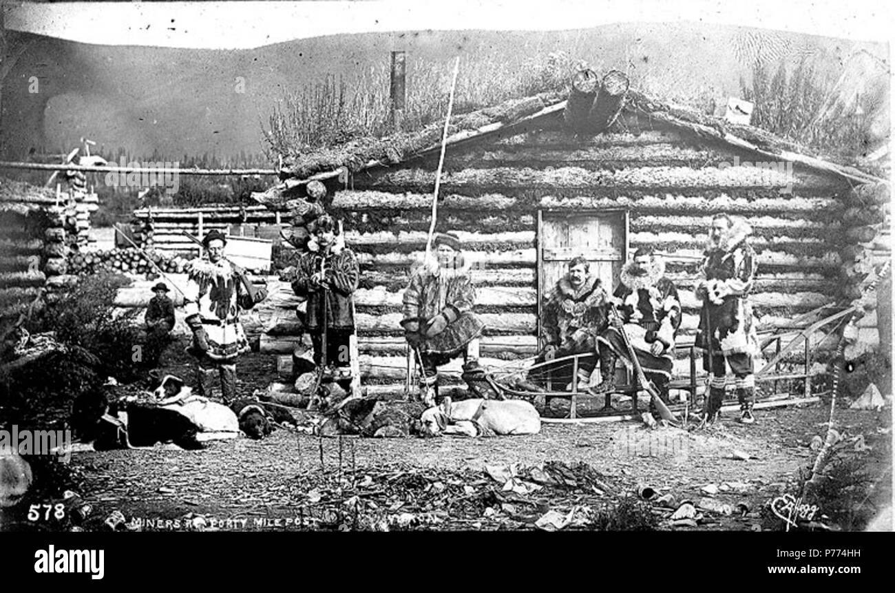 . Inglese: Minatori a Fortymile Post, Yukon Territory, ca. 1898. Inglese: mostra sei uomini vestiti di pelli e pellicce che trasportano le pistole in piedi di fronte a log cabin con dogsled . Didascalia sulla immagine: 'Miners a quaranta miglia di Post Yukon' Klondike Gold Rush. Soggetti (LCTGM): Gold Miner--Yukon--Fortymile; indumenti di pelliccia--Yukon--Fortymile; edifici Log--Yukon--Fortymile . circa 1898 9 minatori a Fortymile Post, Yukon Territory, ca 1898 (HEGG 451) Foto Stock