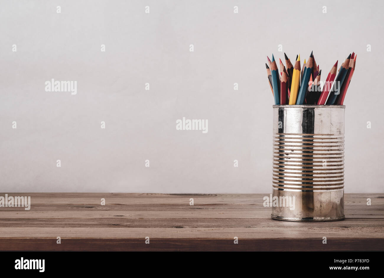Una varietà di matite colorate in un vecchio stagno metallico su un asse di legno scrivania con copia spazio a sinistra e sopra. Filtrato per effetto retrò. Foto Stock