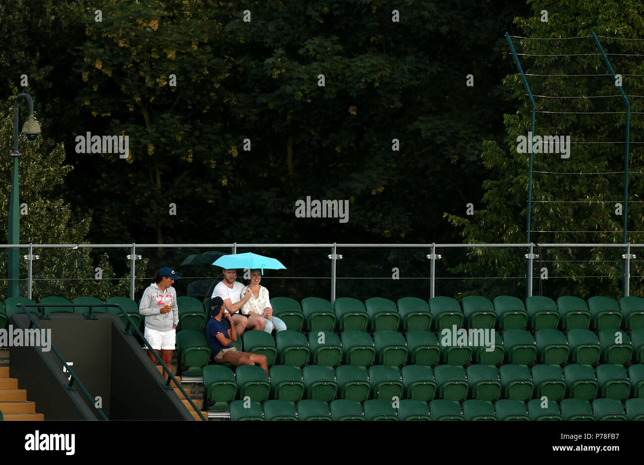 Spettatori riparo dalla pioggia sulla corte due durante un ritardo di pioggia il giorno tre i campionati di Wimbledon al All England Lawn Tennis e Croquet Club, Wimbledon. Foto Stock