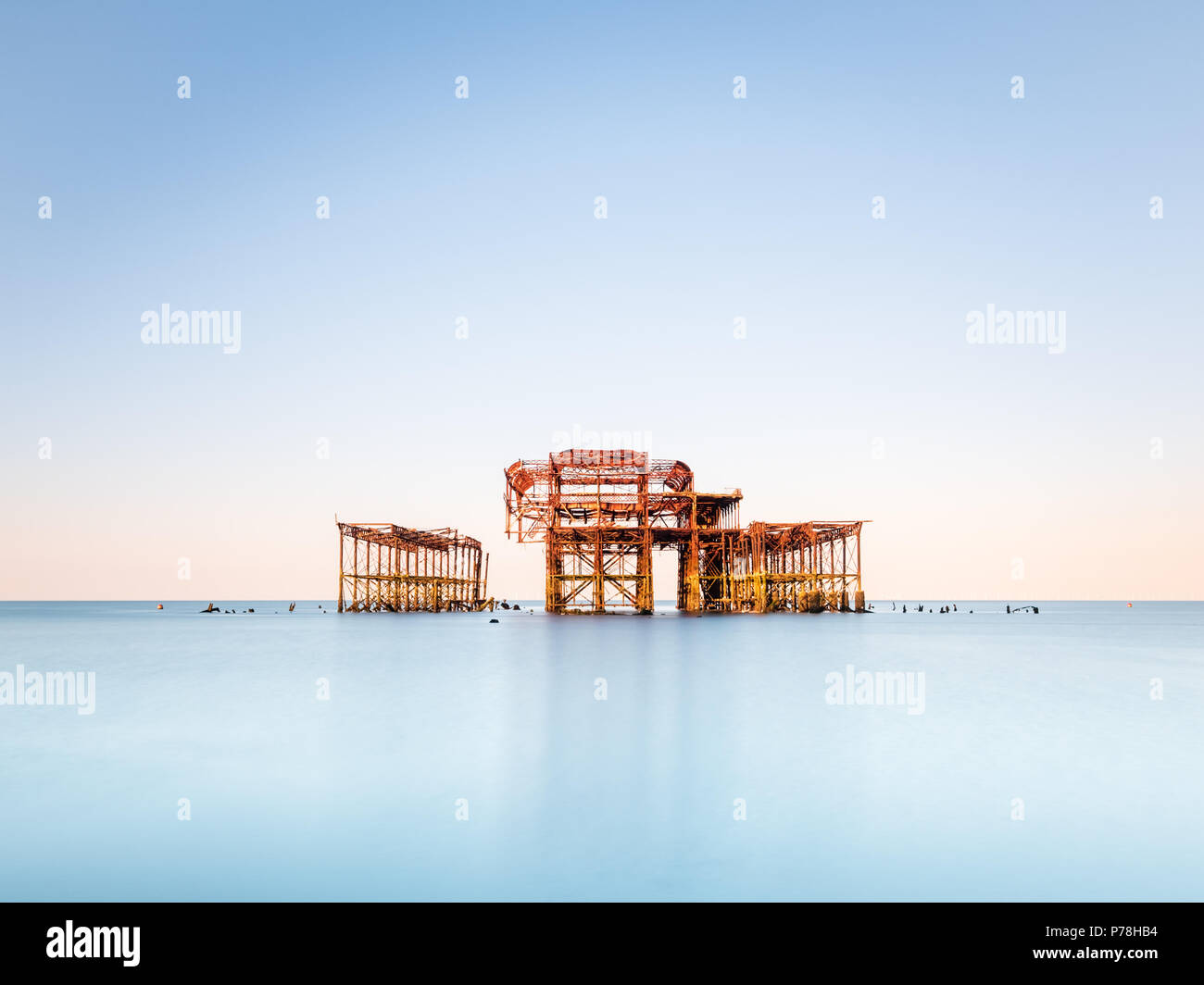 In stile minimalista Molo Ovest di Brighton, East Sussex, a sunrise e riflessa in un mare calmo con belle sfumature pastello in un cielo privo di nuvole Foto Stock