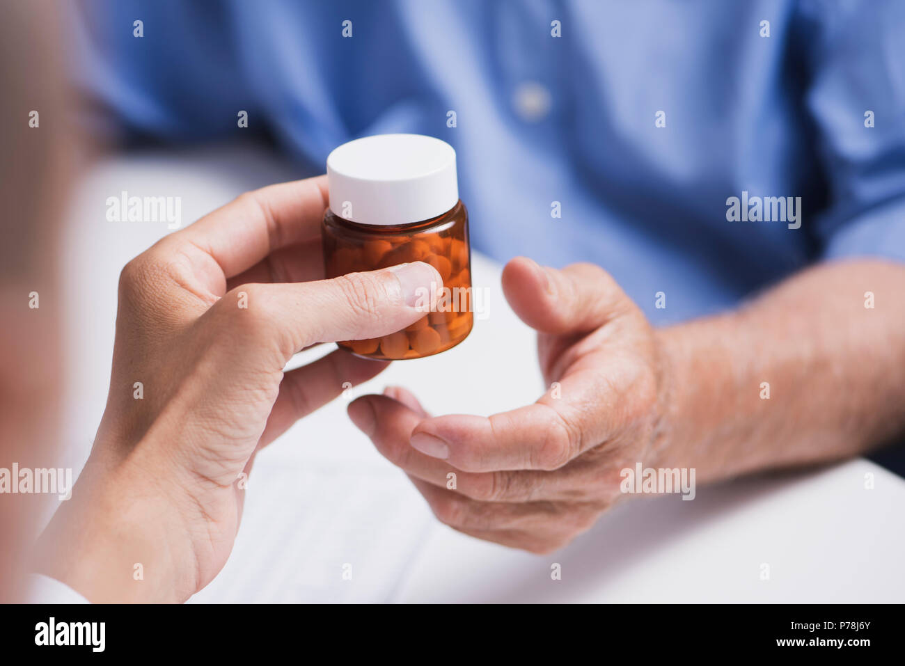 Primo piano di un medico caucasica uomo in camice bianco, dando una bottiglia di pillole a un senior caucasica uomo paziente, seduta sia in corrispondenza di un banco medici Foto Stock