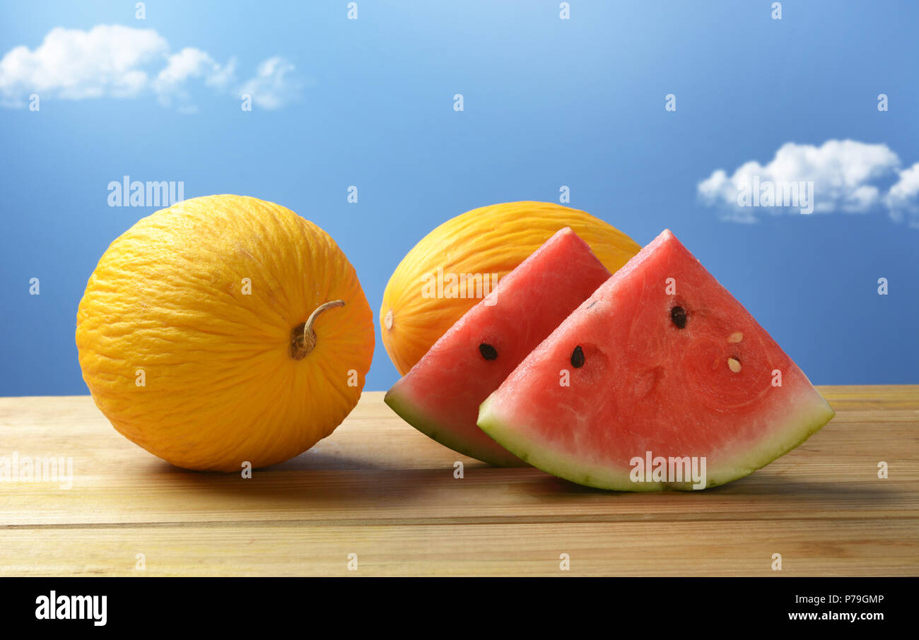 Melone giallo e rosso anguria sul tavolo di legno con cielo blu in background - frutta siciliana - primo piano Foto Stock