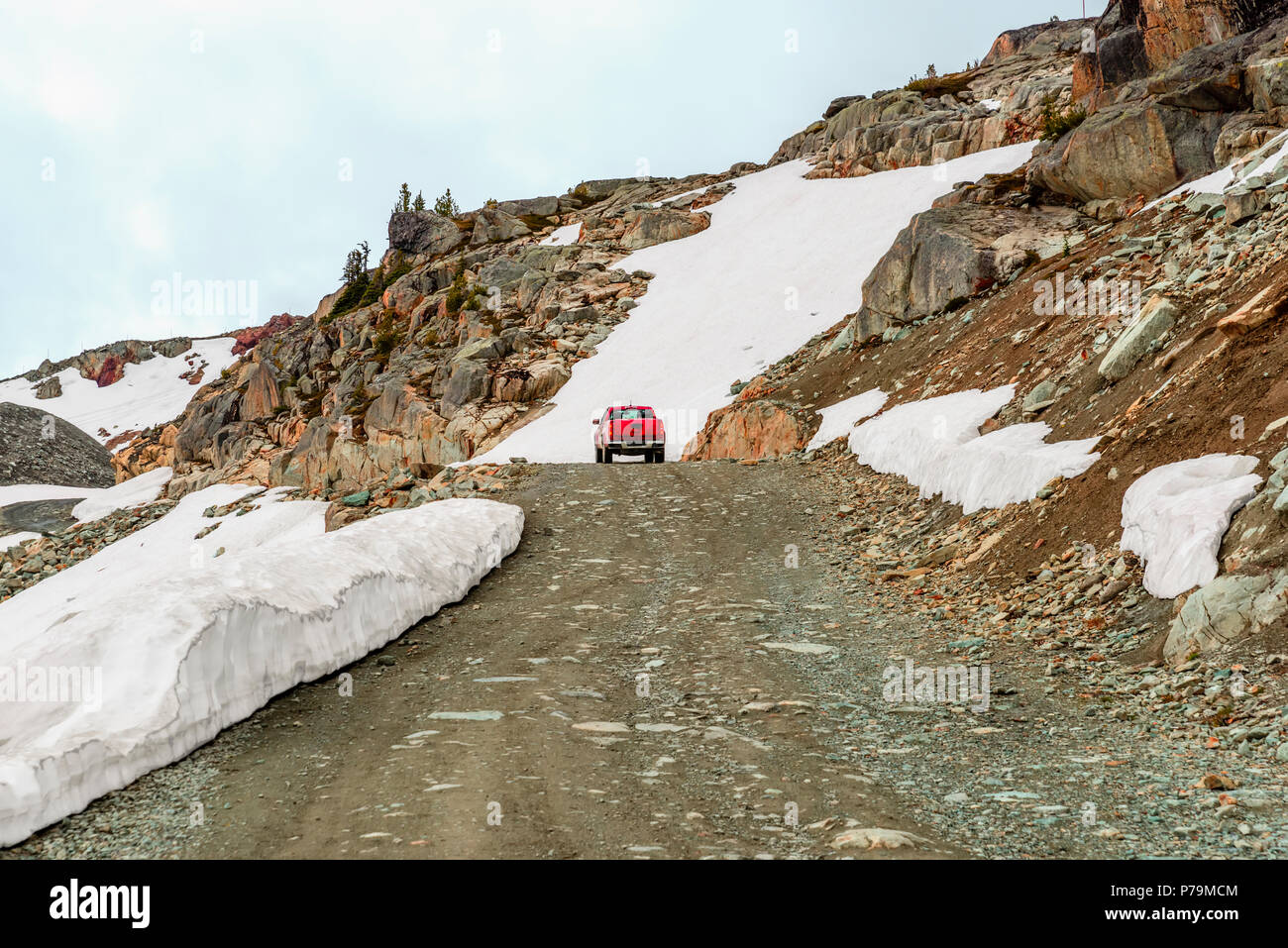 Un rosso corse in auto lungo la strada di un paese nelle montagne rocciose, passato cumuli di neve, nel pomeriggio autunnale Foto Stock