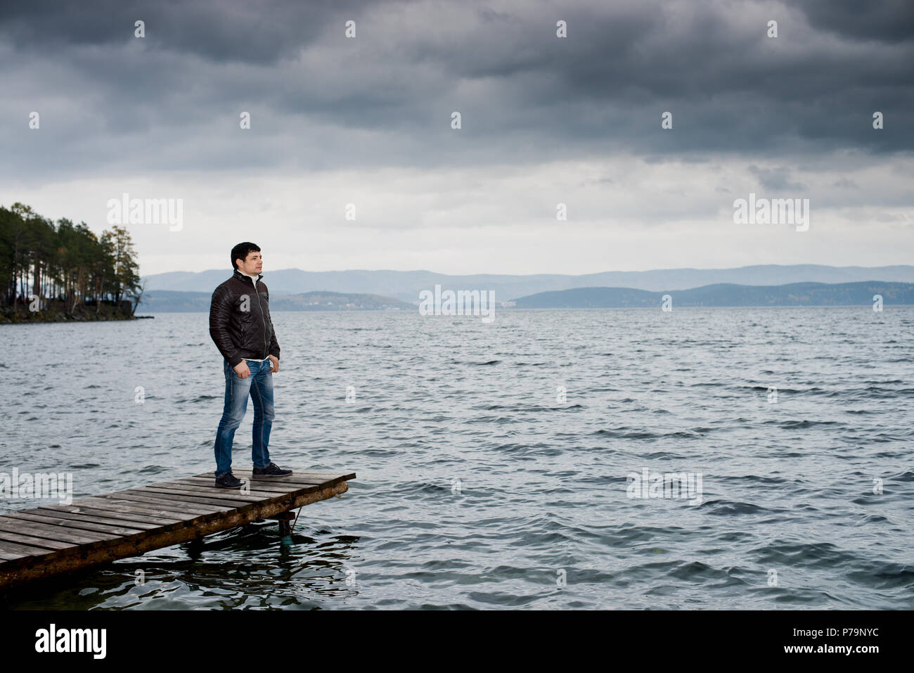 Giovane ragazzo all'aperto sull'acqua' ormeggio per la barca, in autunno freddo giorno nuvoloso Foto Stock