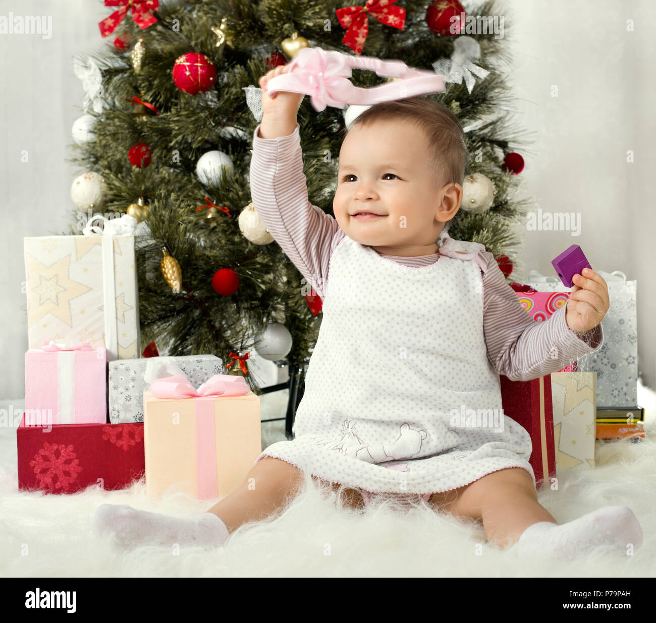 Uno-anno-vecchio bambina solennizzare il Natale, sedersi sotto Natale-albero con il dono Foto Stock