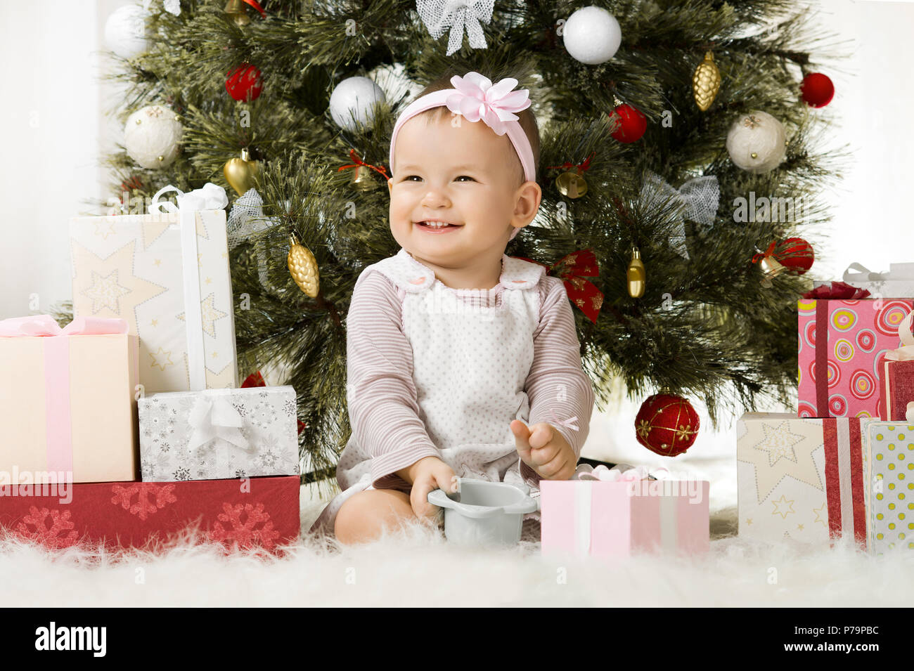 Uno-anno-vecchio bambina solennizzare il Natale, sedersi sotto Natale-albero con il dono Foto Stock