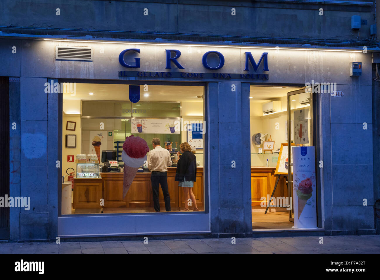 Gelateria Grom Gelateria, strada Nova, Cannaregio, Venezia, Veneto, Italia di notte con vista dalla finestra di una coppia che acquista gelato Foto Stock