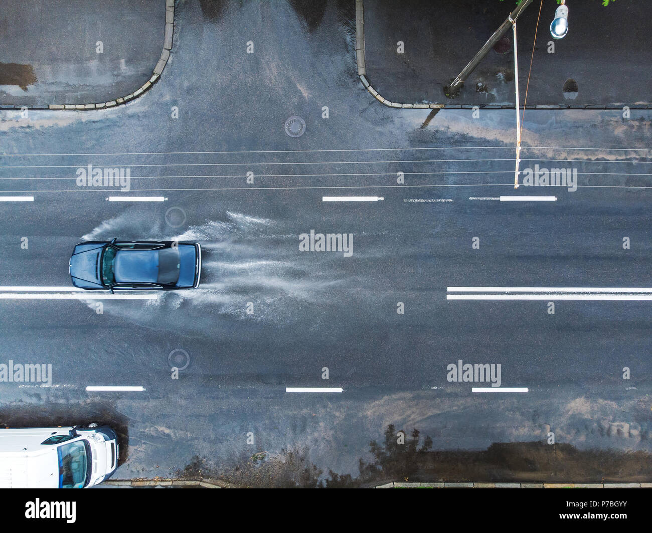 Nero auto schizzi attraverso la grande pozza sulla strada allagata. foto aerea Foto Stock