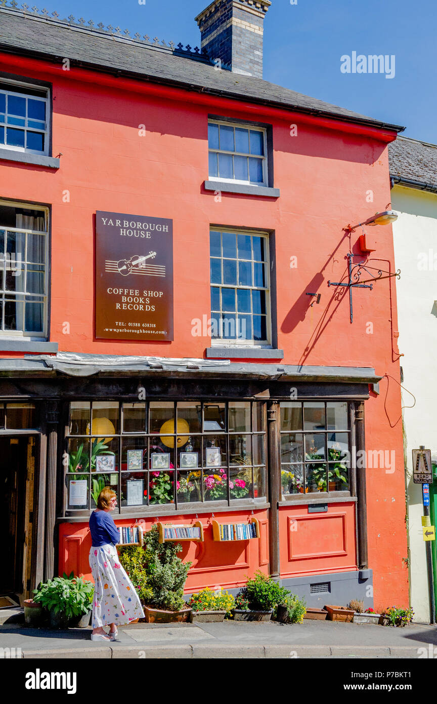 Donna in piedi al di fuori della casa Yarborough second hand book shop e caffetteria nel castello dei vescovi, Shropshire, England, Regno Unito Foto Stock