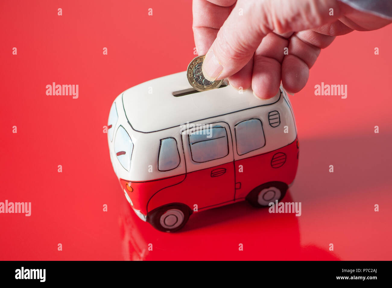 Un risparmiatore mettendo una sterlina britannica moneta nella sua casella di denaro che assomiglia a una VW mini bus Foto Stock
