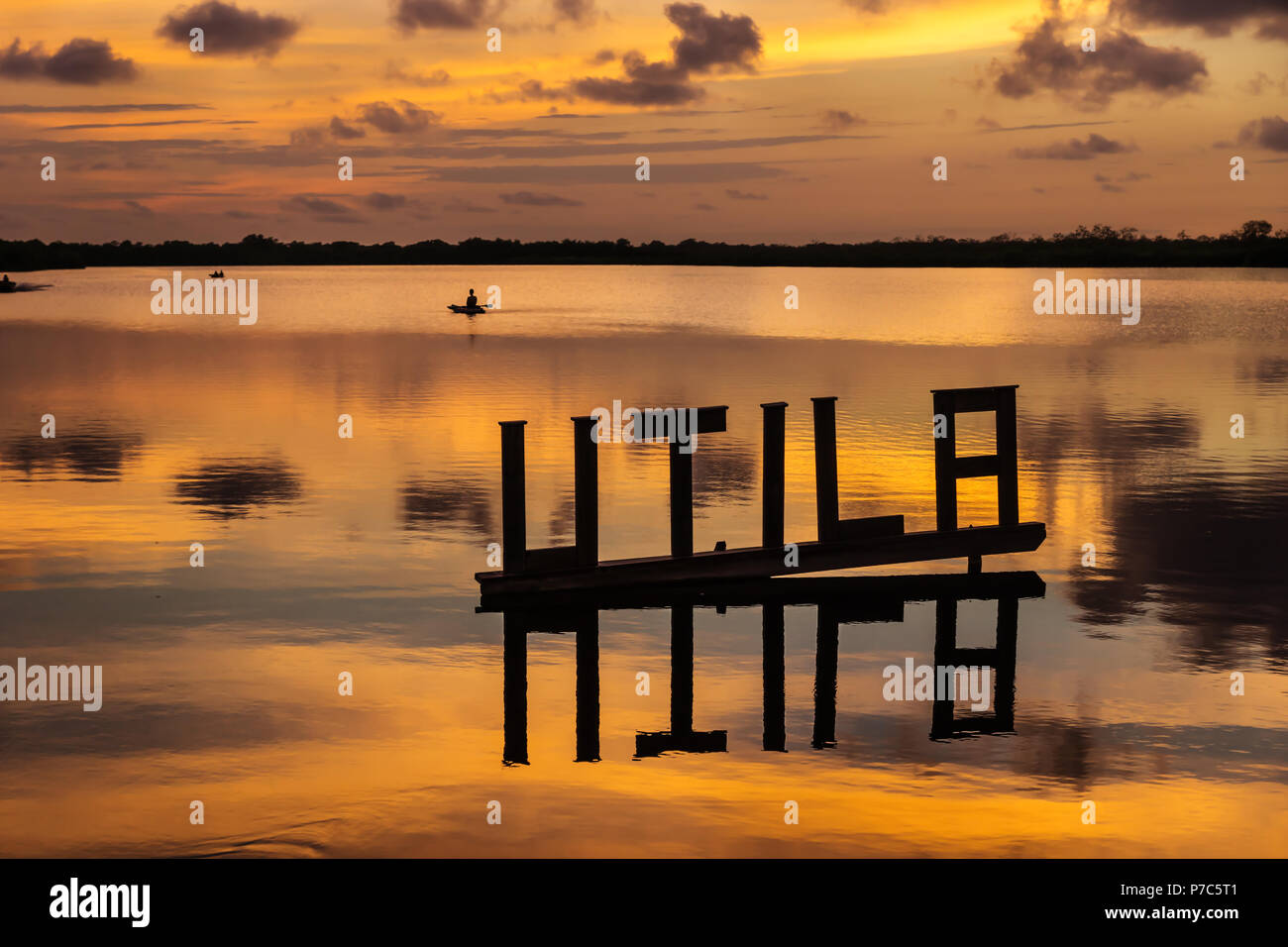 Tramonto a una laguna con lettera Utila segno con kanu in background in colori dorati, Utila, Honduras, America Centrale Foto Stock