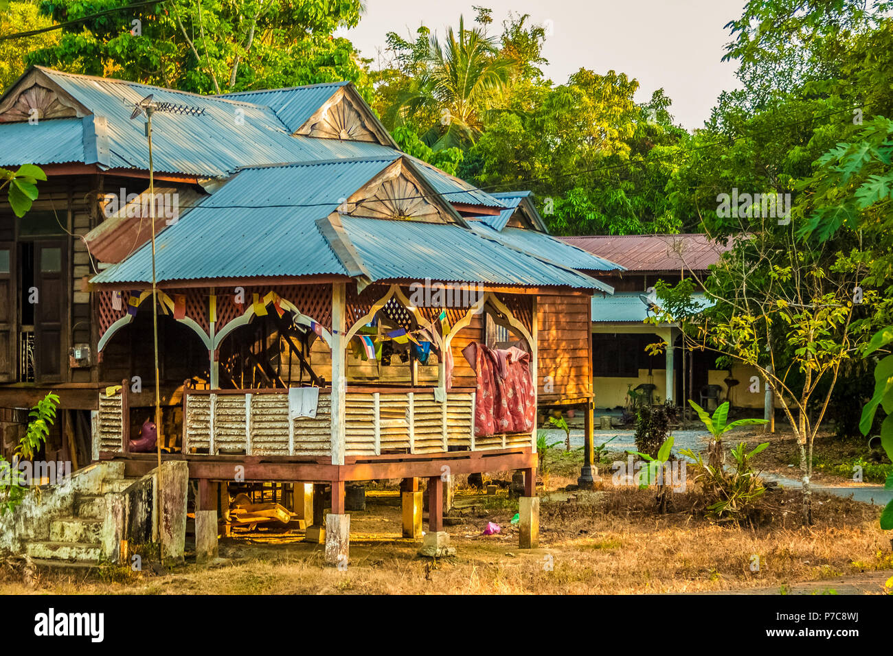 Un tradizionale in legno casa malese su palafitte con giardini tropicali adatta tetto, stendibiancheria su uno stendibiancheria; casa dei residenti locali sull'Isola di Langkawi... Foto Stock