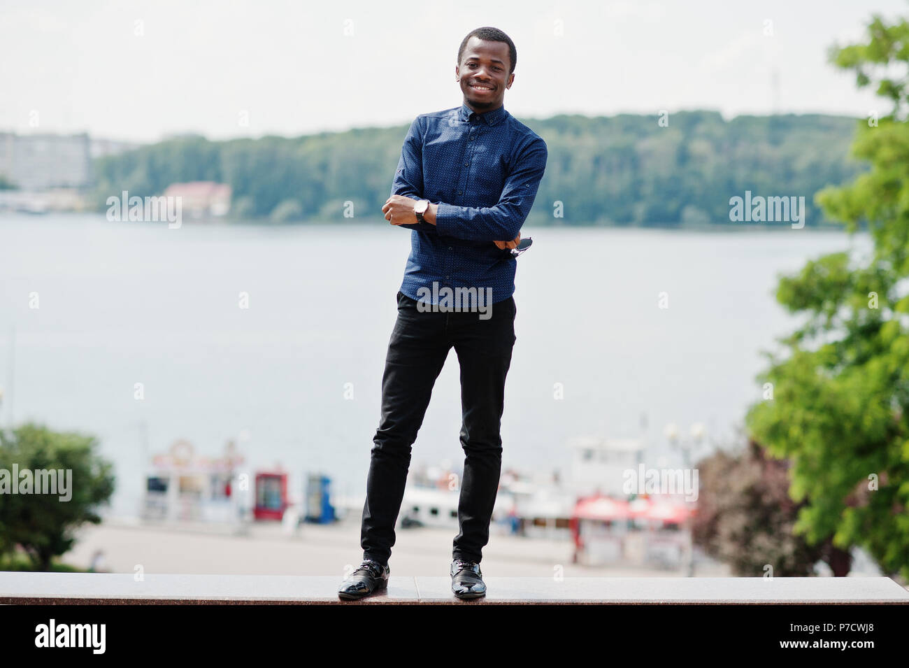 L'uomo africano poste lungo la strada della città di usura sulla maglietta  blu e pantaloni neri Foto stock - Alamy