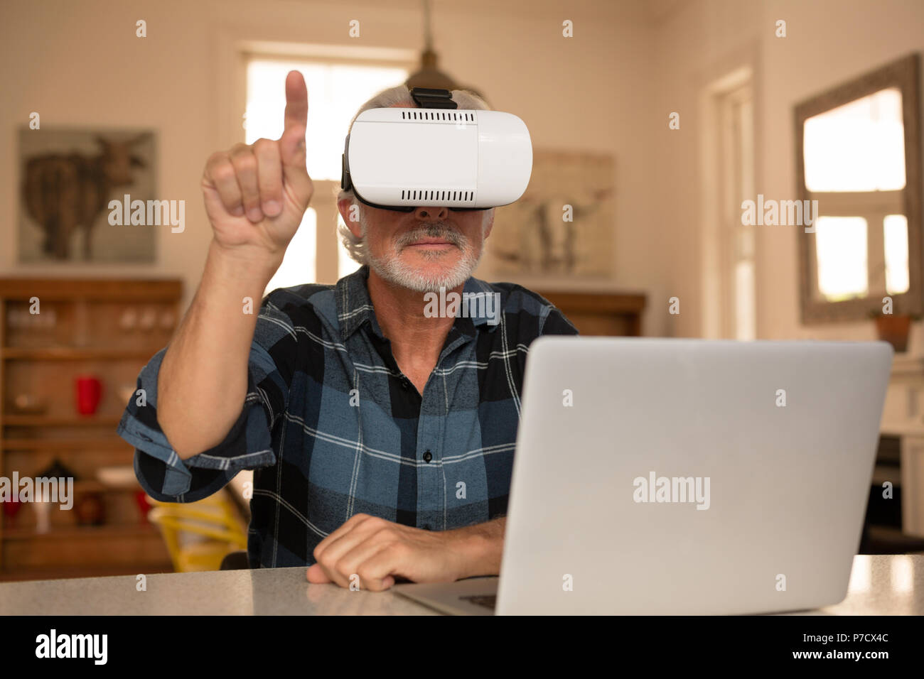 Senior uomo utilizzando la realtà virtuale auricolare con computer portatile in cucina Foto Stock
