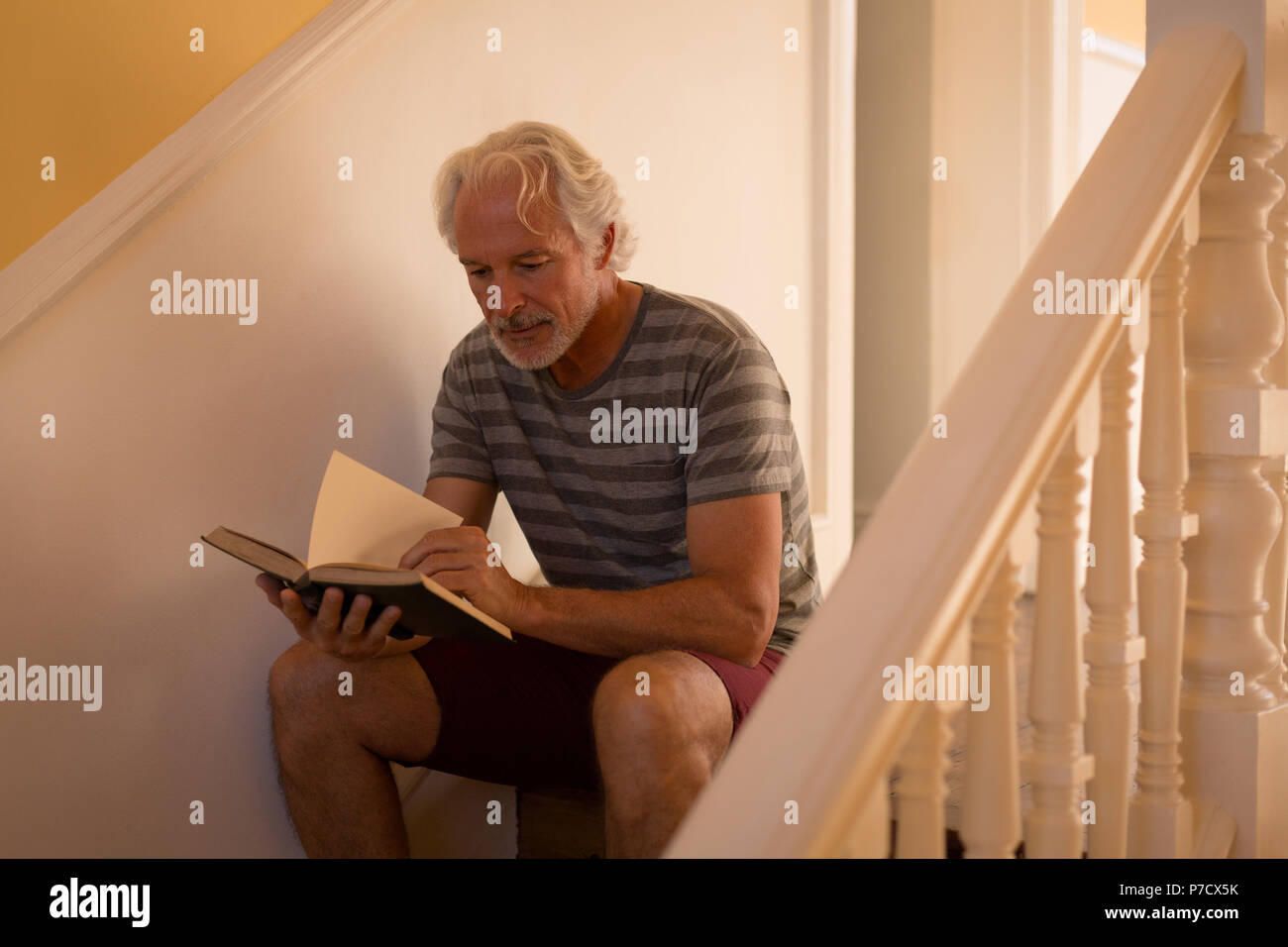 Senior uomo la lettura di un libro su scale a casa Foto Stock