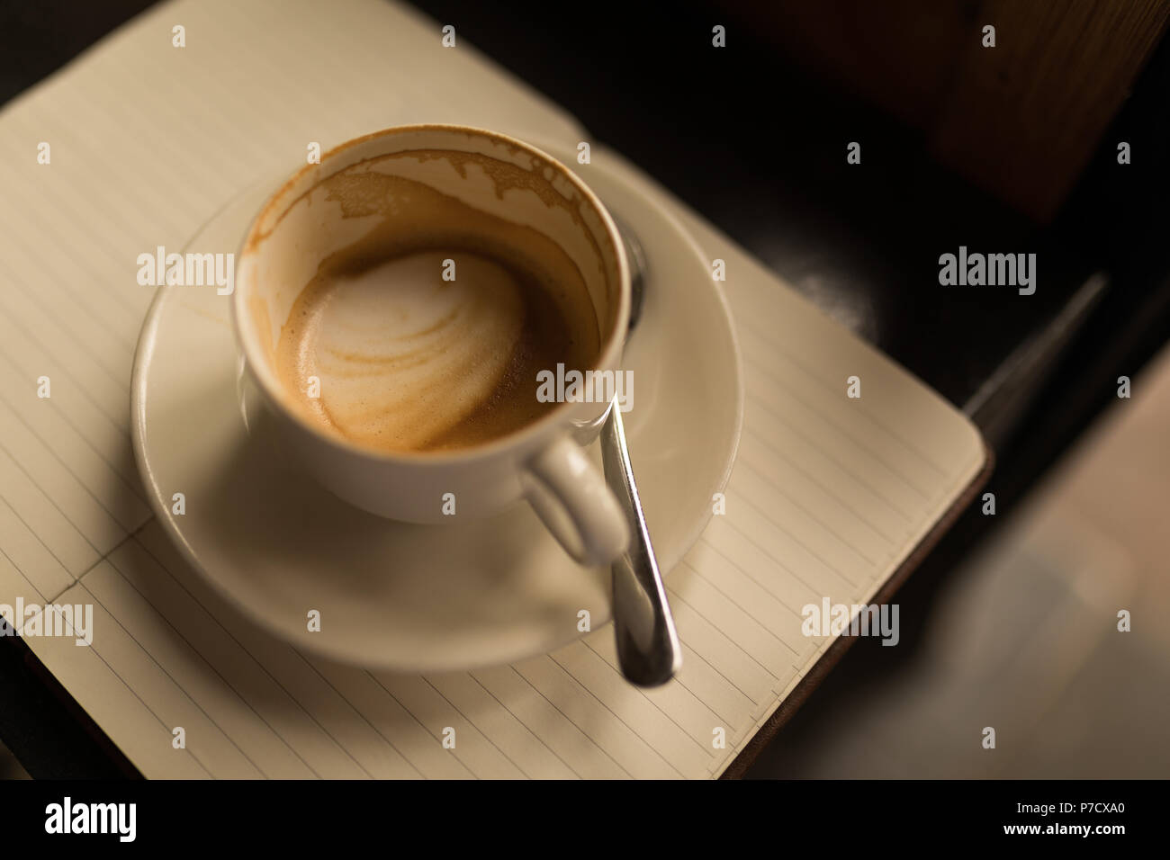Tazza vuota di caffè con piattino e cucchiaio sul diario Foto Stock